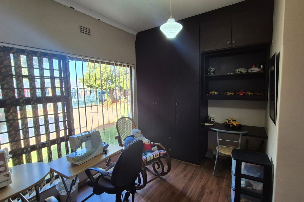 A bedroom featuring built-in dark cabinetry with integrated shelving and desk space, large window with security bars, and wood-look flooring.