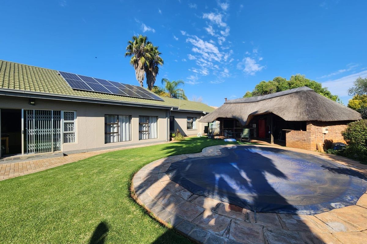 Rear view of the property featuring a swimming pool with cover, a thatched lapa entertainment area, and solar panels installed on the main roof.