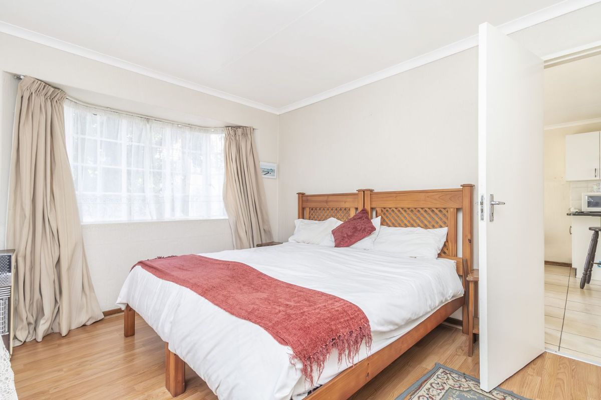 A well-lit bedroom featuring laminate flooring, a large bay window with curtains, and direct access to the adjacent kitchen area.