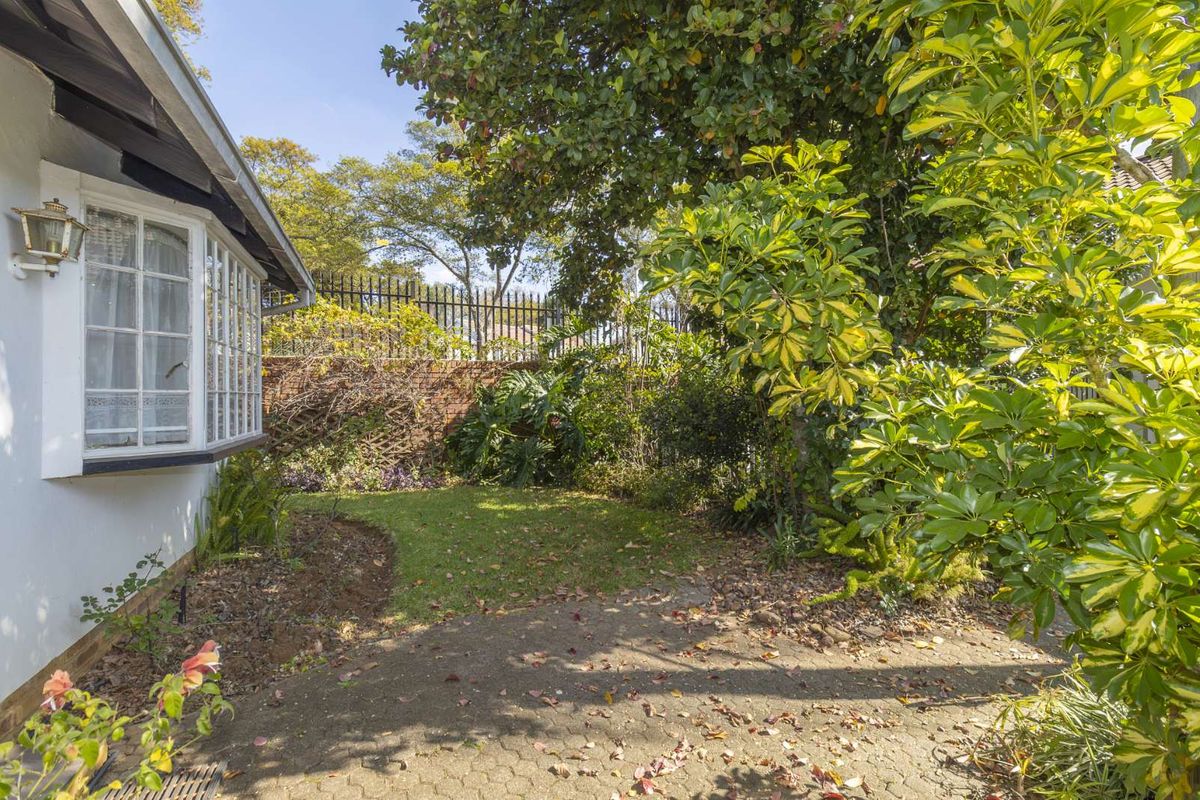A private rear garden area featuring a paved patio, established trees, and a brick boundary wall with security fencing.
