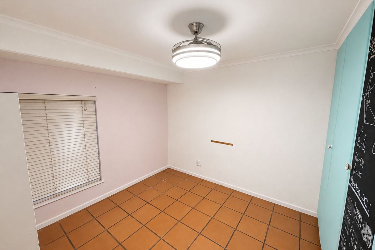 A bright, empty bedroom featuring terracotta floor tiles, a modern ceiling fan light fixture, and built-in cabinetry with a chalkboard finish.