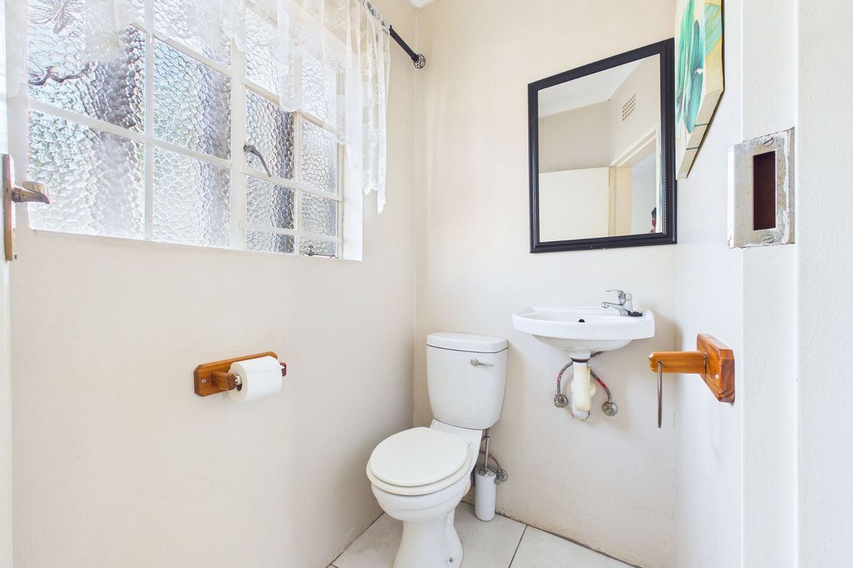 A functional guest bathroom featuring a standard toilet, wall-mounted basin, and textured glass window providing natural light.