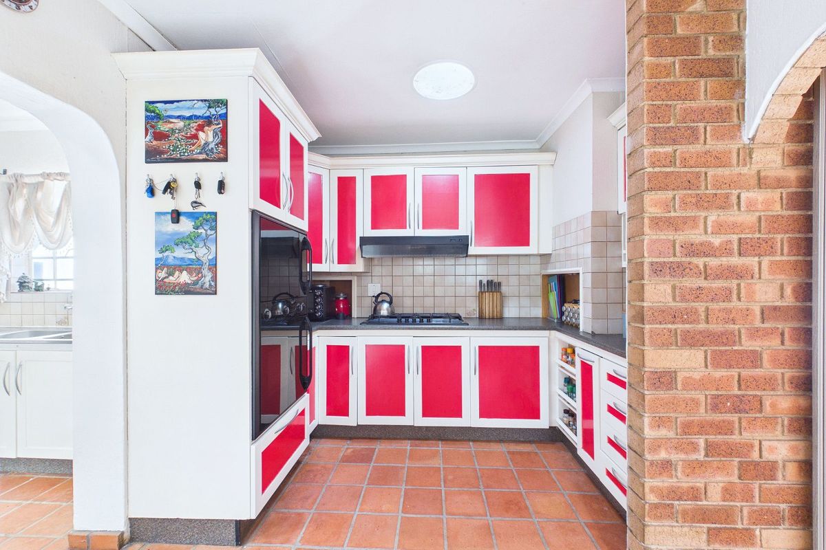 A functional kitchen featuring red and white cabinetry, a built-in oven, gas hob, extractor fan, and terracotta floor tiles.