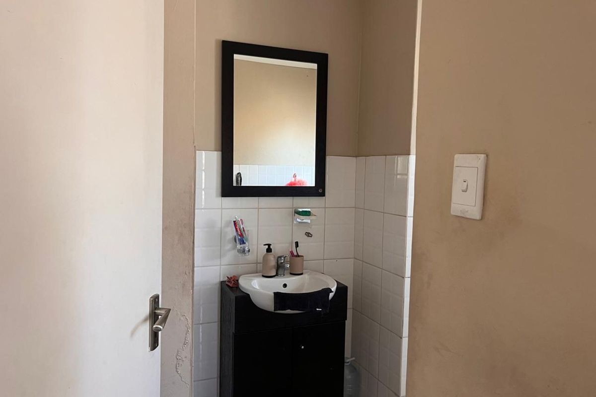 A compact bathroom featuring a wall-mounted mirror, a small vanity cabinet with a basin, and tiled splashback area.