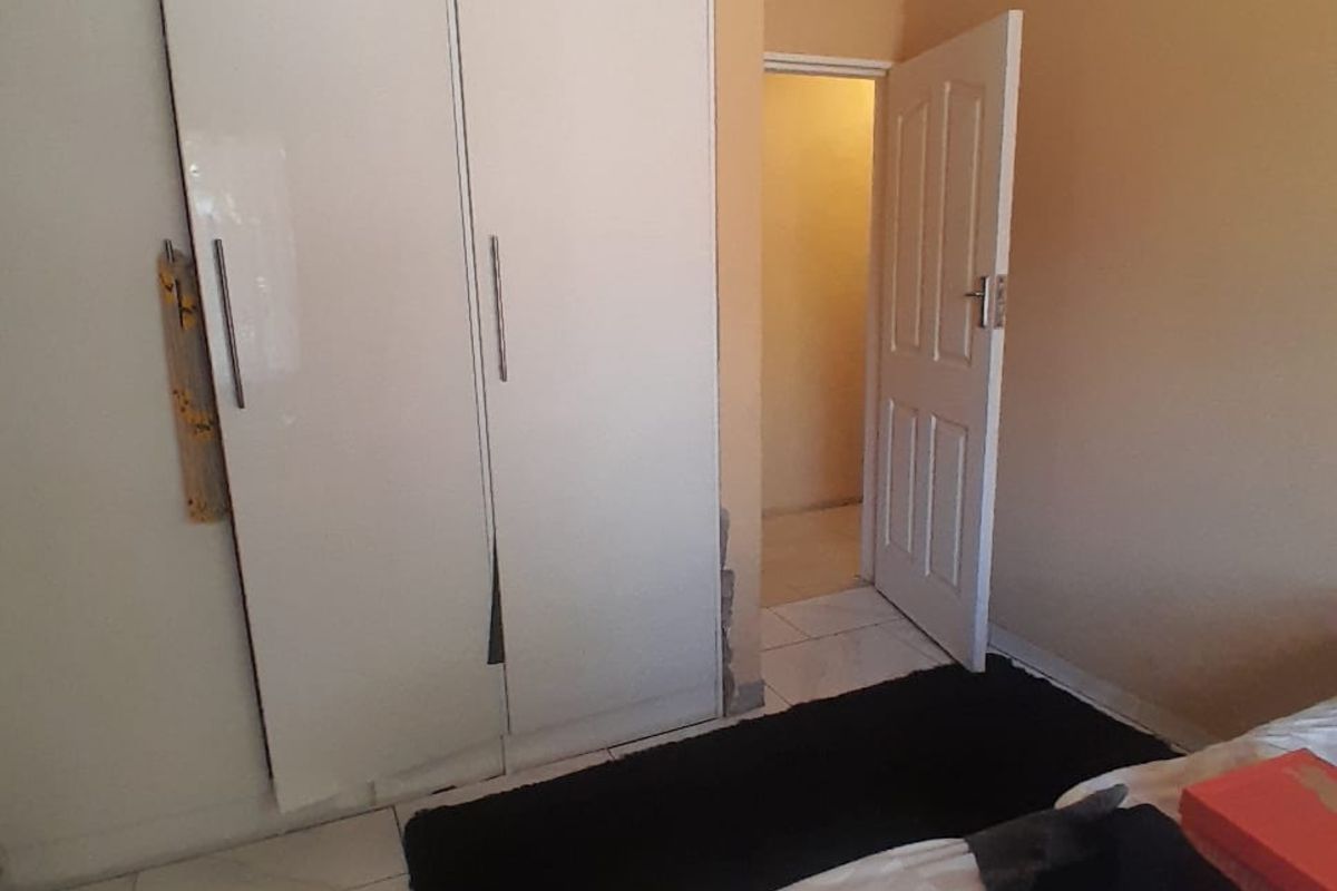 A bedroom featuring built-in wardrobes, tiled flooring, and decorative ceiling cornices, leading to an adjacent hallway.