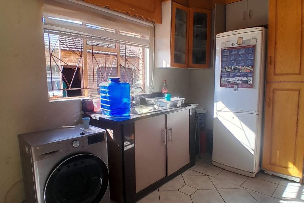 A functional kitchen area featuring wooden cabinetry, tiled flooring, and a window with security bars, providing a practical space for daily tasks.