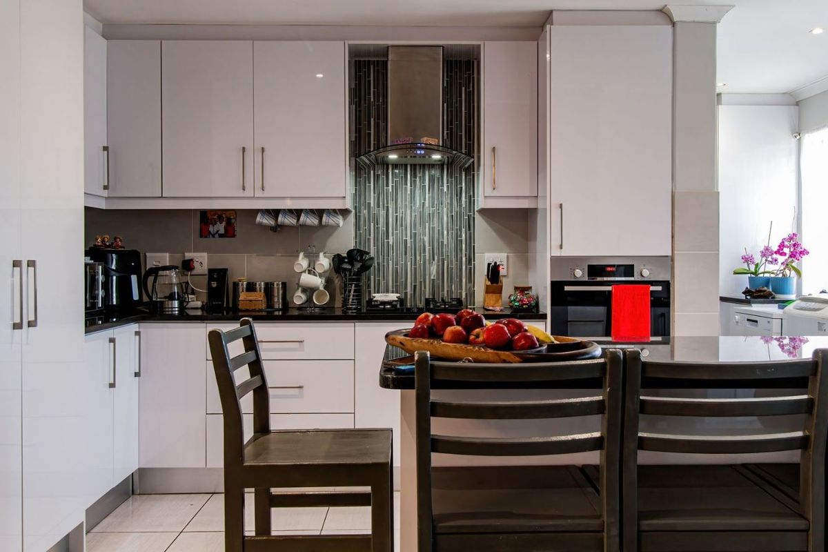 Modern kitchen featuring white cabinetry, dark countertops, a tiled backsplash, built-in oven, and a stainless steel extractor fan.