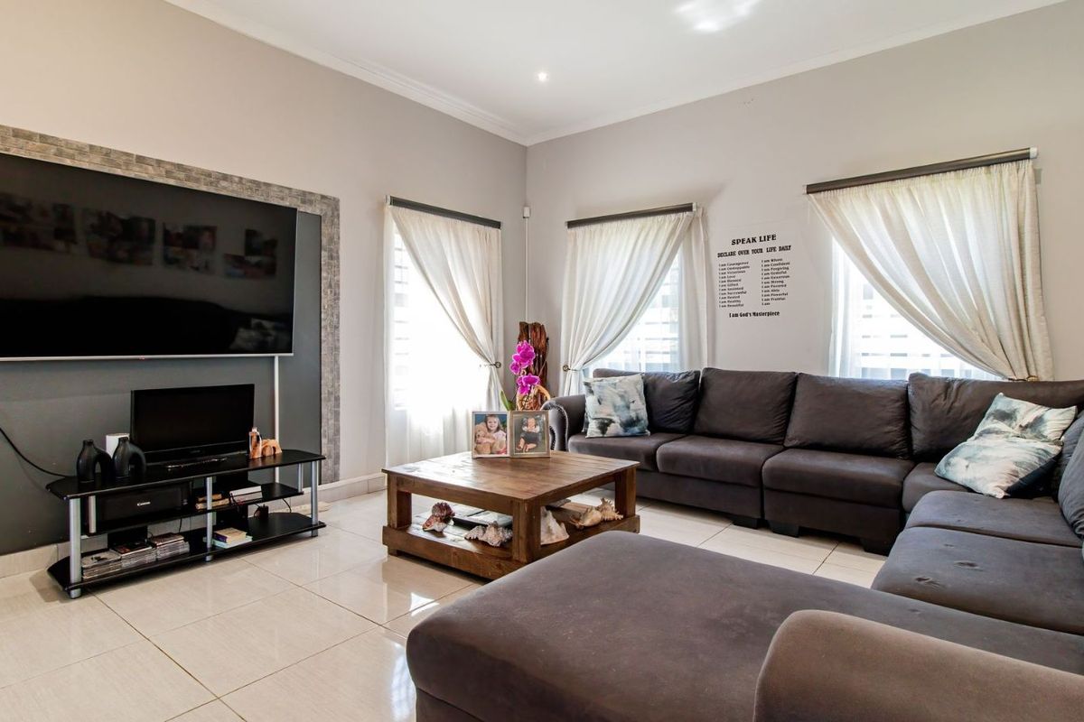 A spacious living room featuring large format floor tiles, recessed downlighting, and a feature wall with stone-look tiling surrounding the television area.