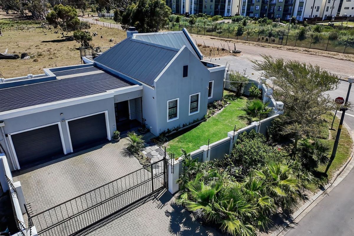 Aerial view of a modern house featuring a double garage, paved driveway, landscaped garden, and a corrugated metal roof.