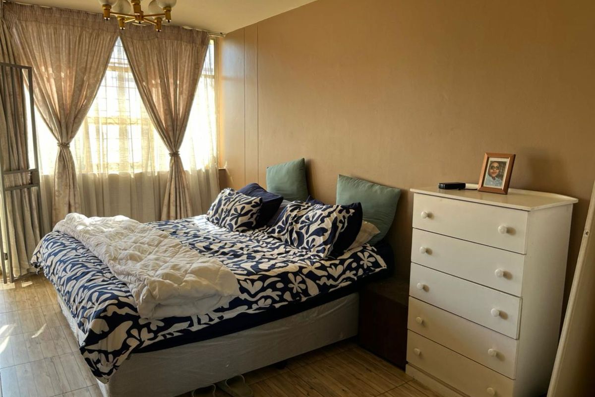 A bedroom featuring tiled flooring, a large window with curtains, and a central ceiling light fixture.