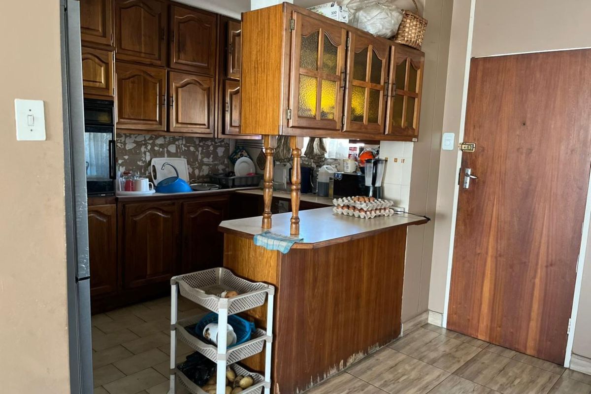 A dated kitchen featuring traditional wooden cabinetry, a breakfast counter, and tiled flooring, offering potential for a modern renovation.