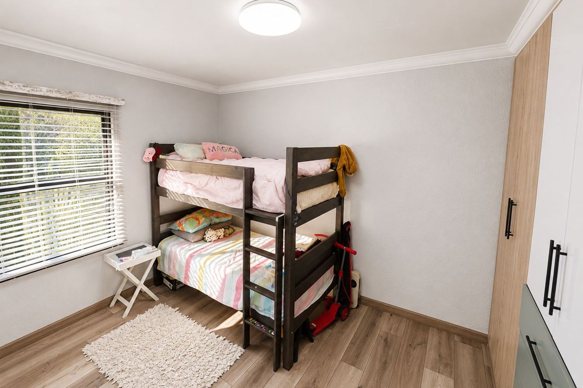 A bright bedroom featuring wood-look laminate flooring, built-in cabinetry, and a large window with fitted blinds.