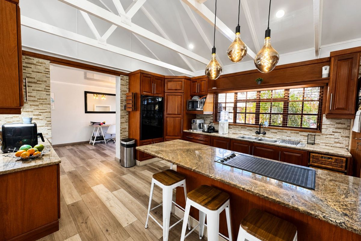 Spacious kitchen featuring rich timber cabinetry, granite countertops, a central island with integrated cooktop, and vaulted ceilings with exposed beams.