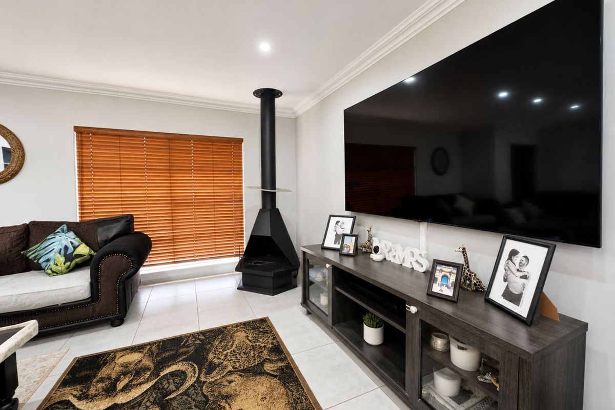 A bright living room featuring a modern freestanding black fireplace, tiled flooring, and large wall-mounted television.