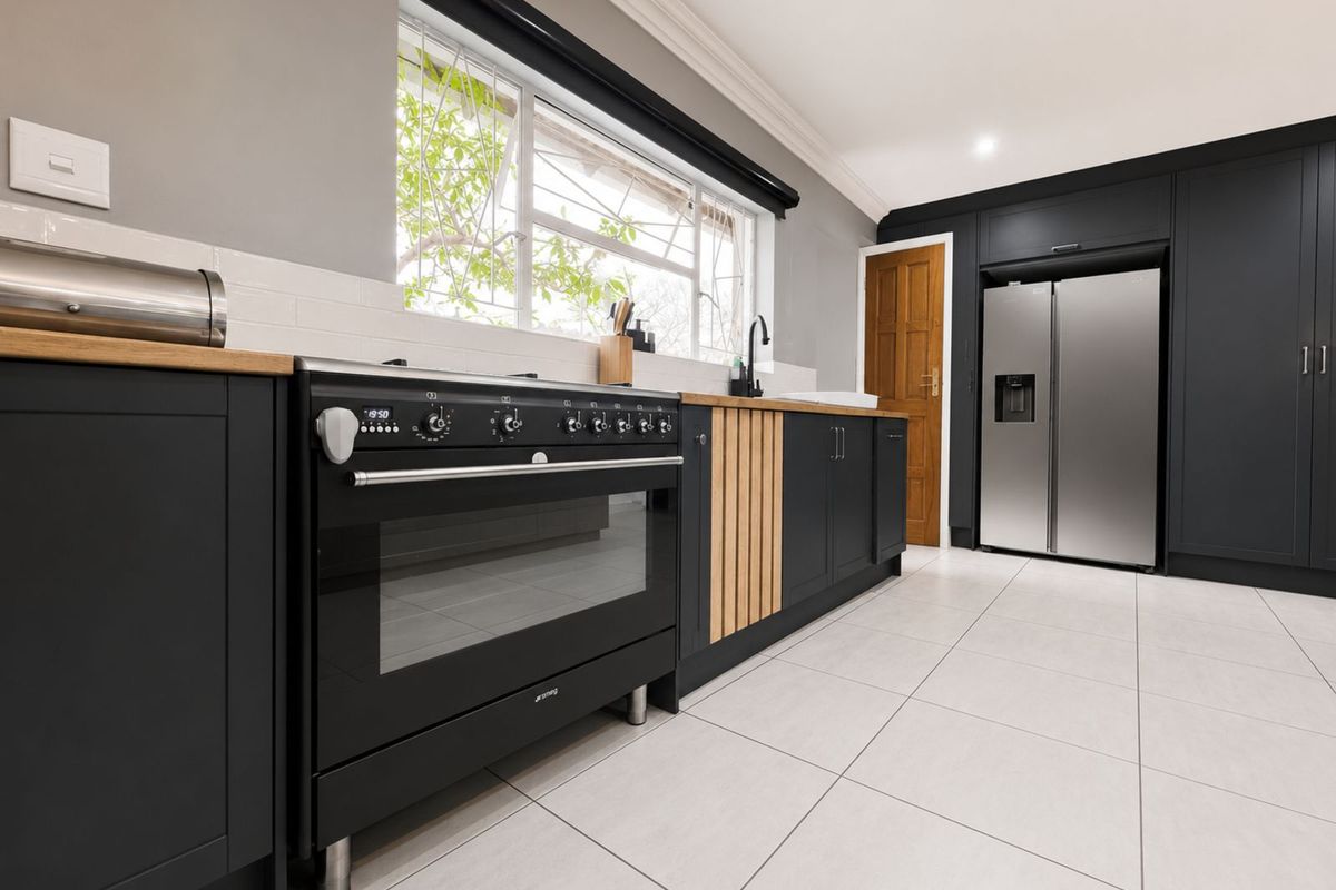 Modern kitchen featuring dark cabinetry, timber countertops, a large freestanding oven, and light-colored floor tiles.