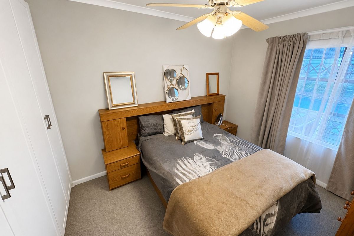 A well-maintained bedroom featuring built-in wooden headboard cabinetry, integrated bedside storage, and white built-in cupboards with a ceiling fan.