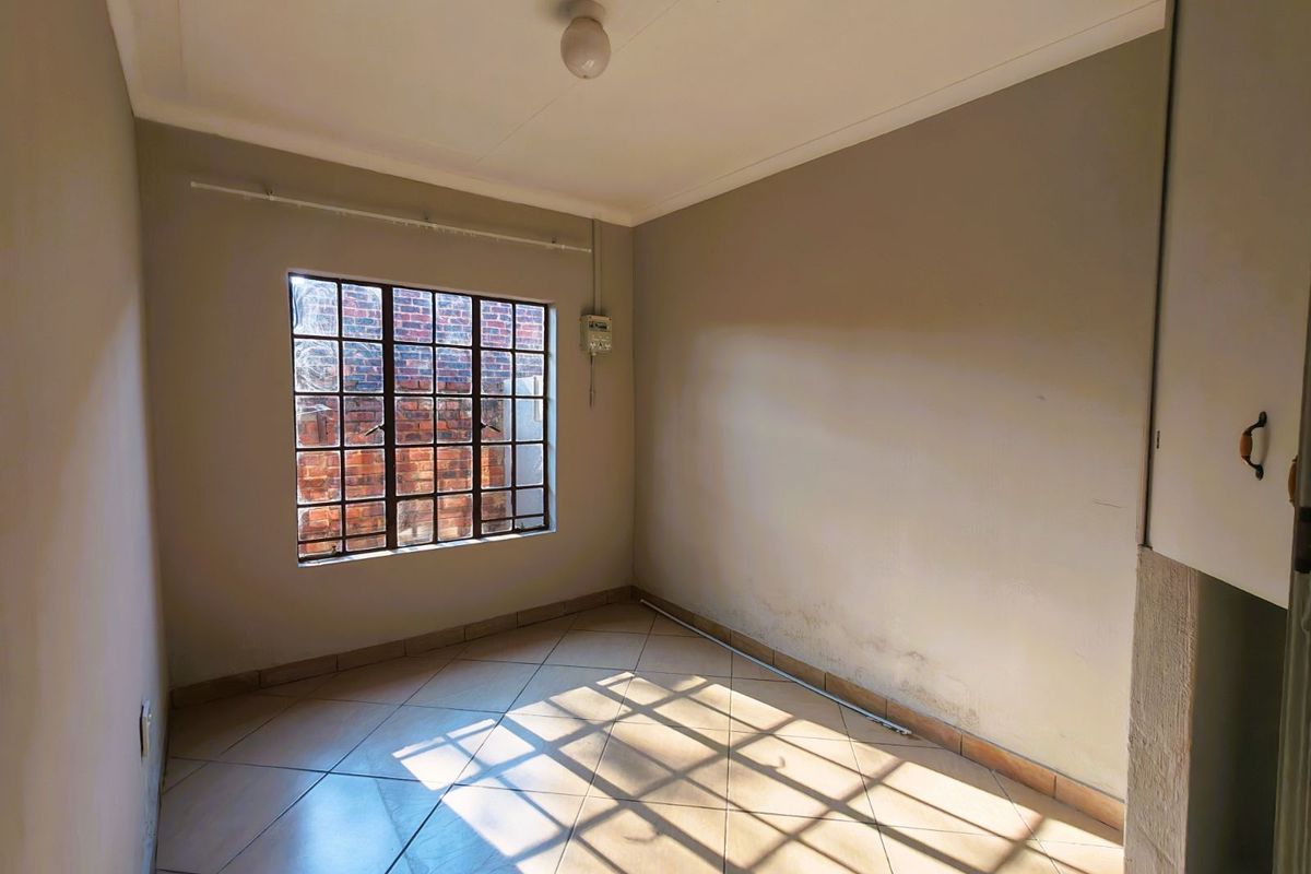A vacant bedroom featuring tiled flooring, a metal-framed window with security bars, and built-in cupboard storage.
