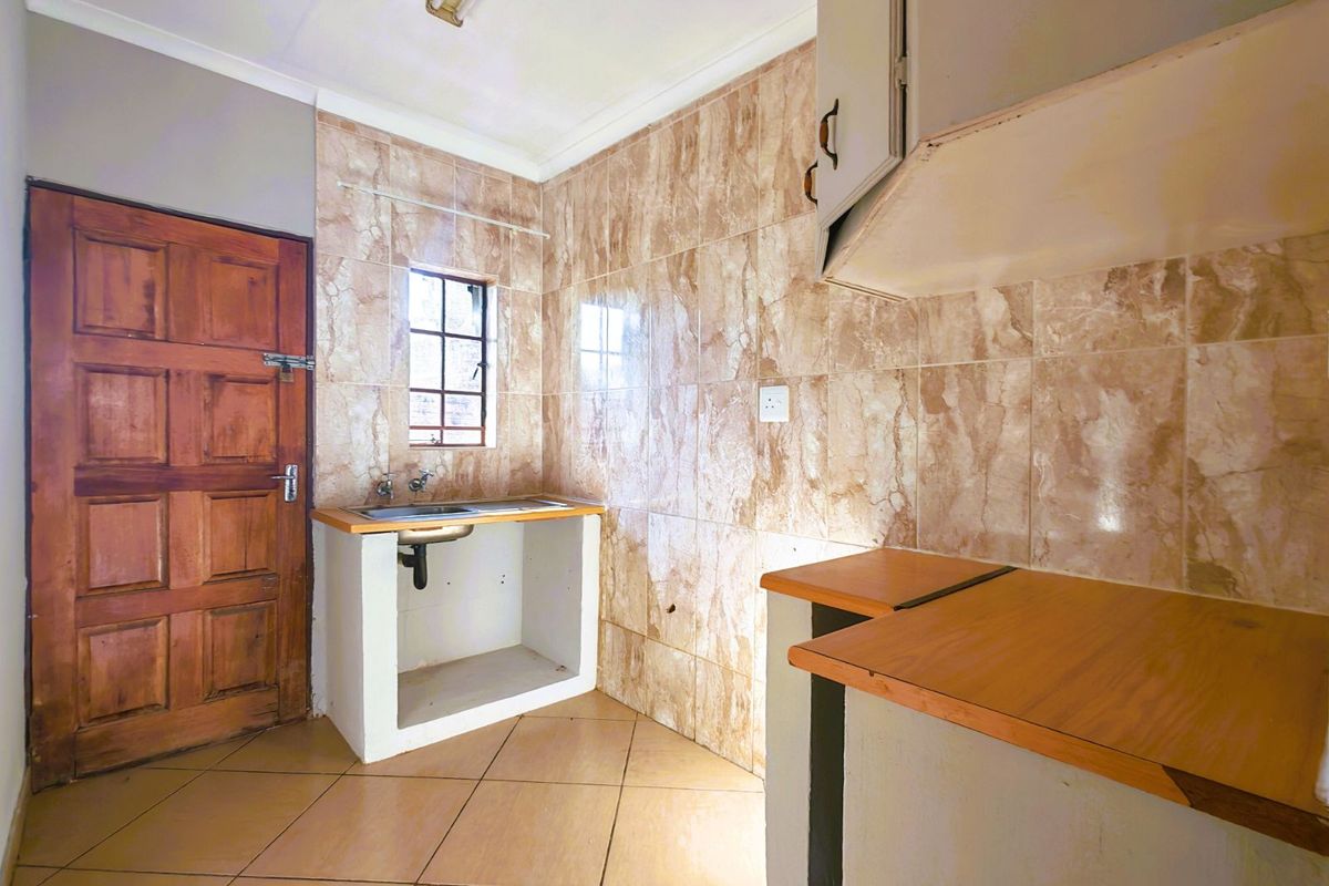 A compact kitchen area featuring tiled walls, a single sink basin, and basic built-in counter structures with wooden tops.