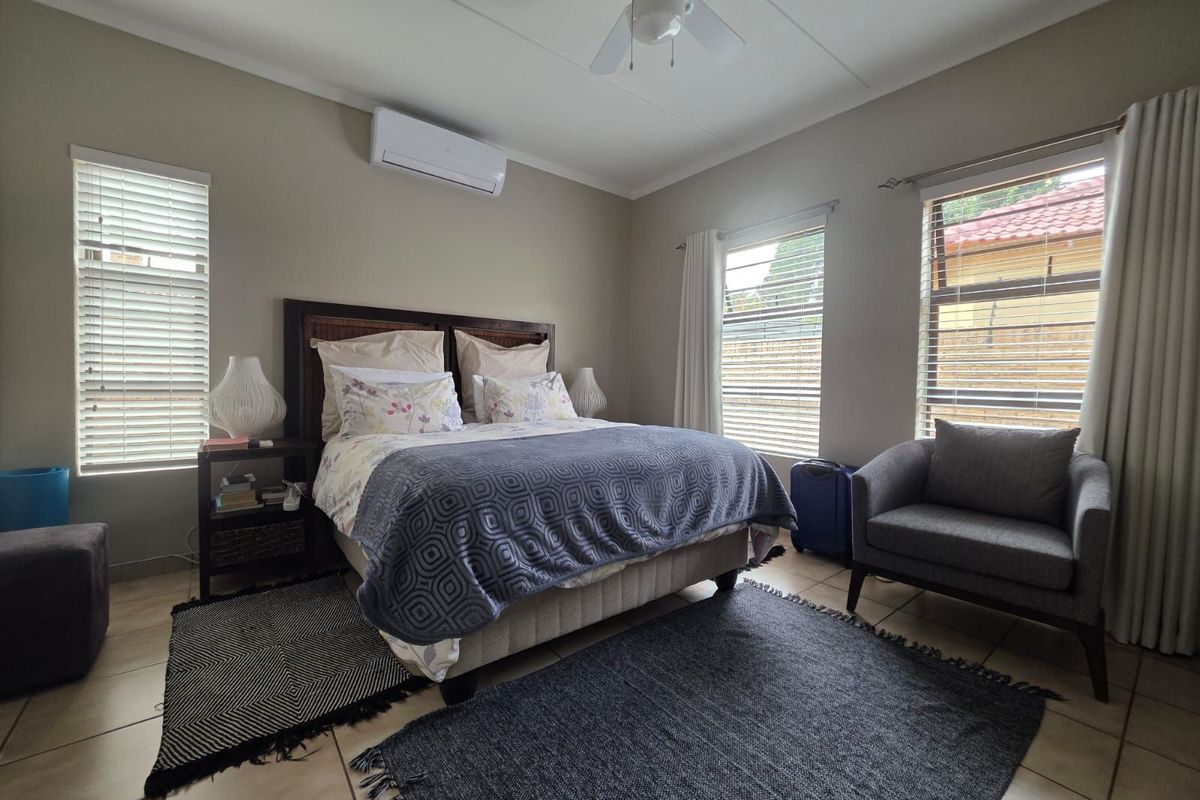 A well-lit bedroom featuring tiled flooring, a wall-mounted air conditioning unit, and a ceiling fan, providing a comfortable and functional living space.