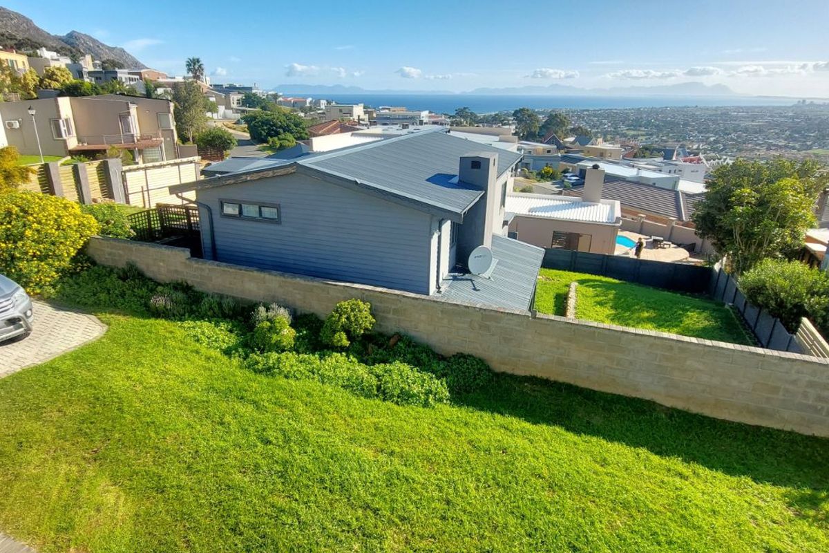 Aerial view of a residential property featuring a metal roof, chimney, and a spacious lawn with a boundary wall and distant coastal views.