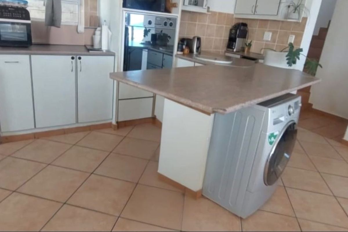 Functional kitchen featuring tiled flooring, laminate countertops, built-in cabinetry, and integrated laundry appliances, offering a practical layout with potential for modern updates.