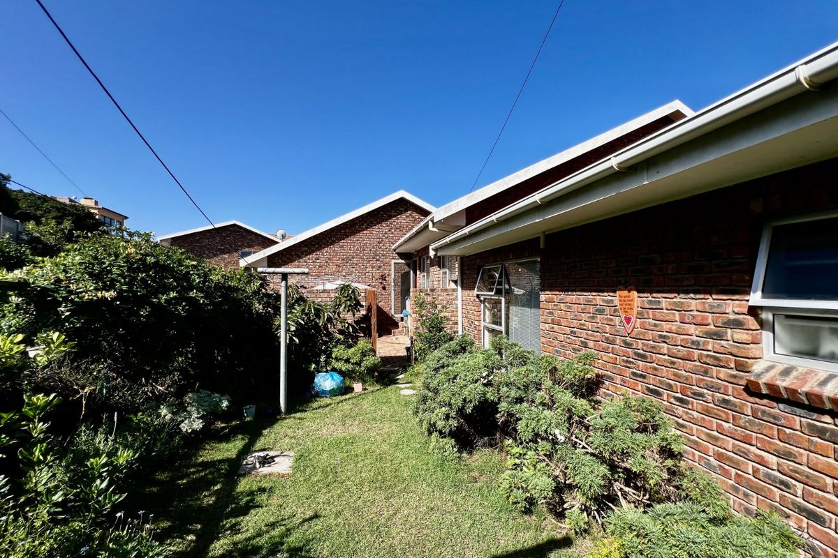 A view of the rear exterior of the house, featuring exposed brick walls, a small lawn area, and established garden landscaping.