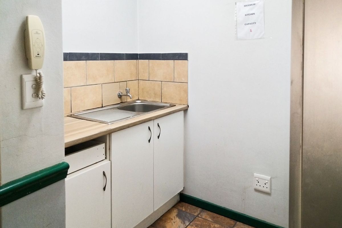 A compact office kitchenette featuring a stainless steel sink, laminate countertop, white cabinetry, and tiled backsplash.