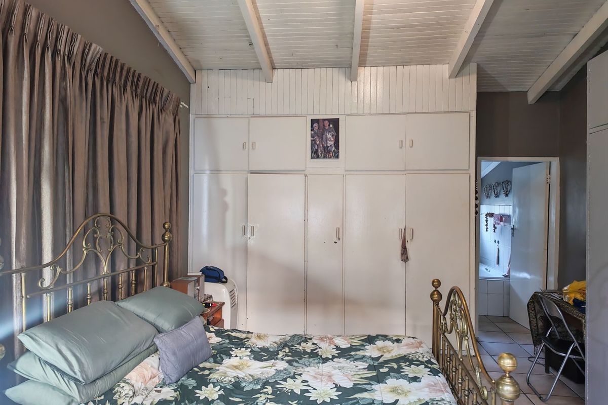 A bedroom featuring built-in cupboards, exposed beam ceiling, and an adjoining bathroom, offering a functional layout with potential for cosmetic updates.