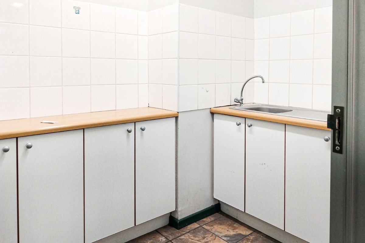 A functional kitchenette area featuring white cabinetry, light wood-look countertops, a stainless steel sink, and white tiled splashbacks.