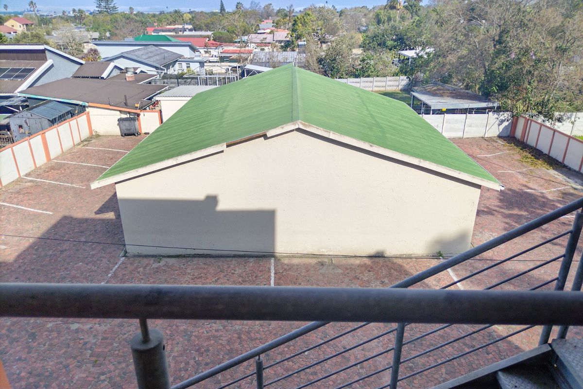 Elevated view overlooking a paved parking area with marked bays and a detached building featuring a green pitched roof.