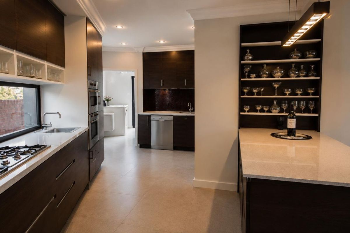 Modern kitchen featuring dark wood cabinetry, stone countertops, integrated appliances, and a dedicated display shelving unit with recessed lighting.