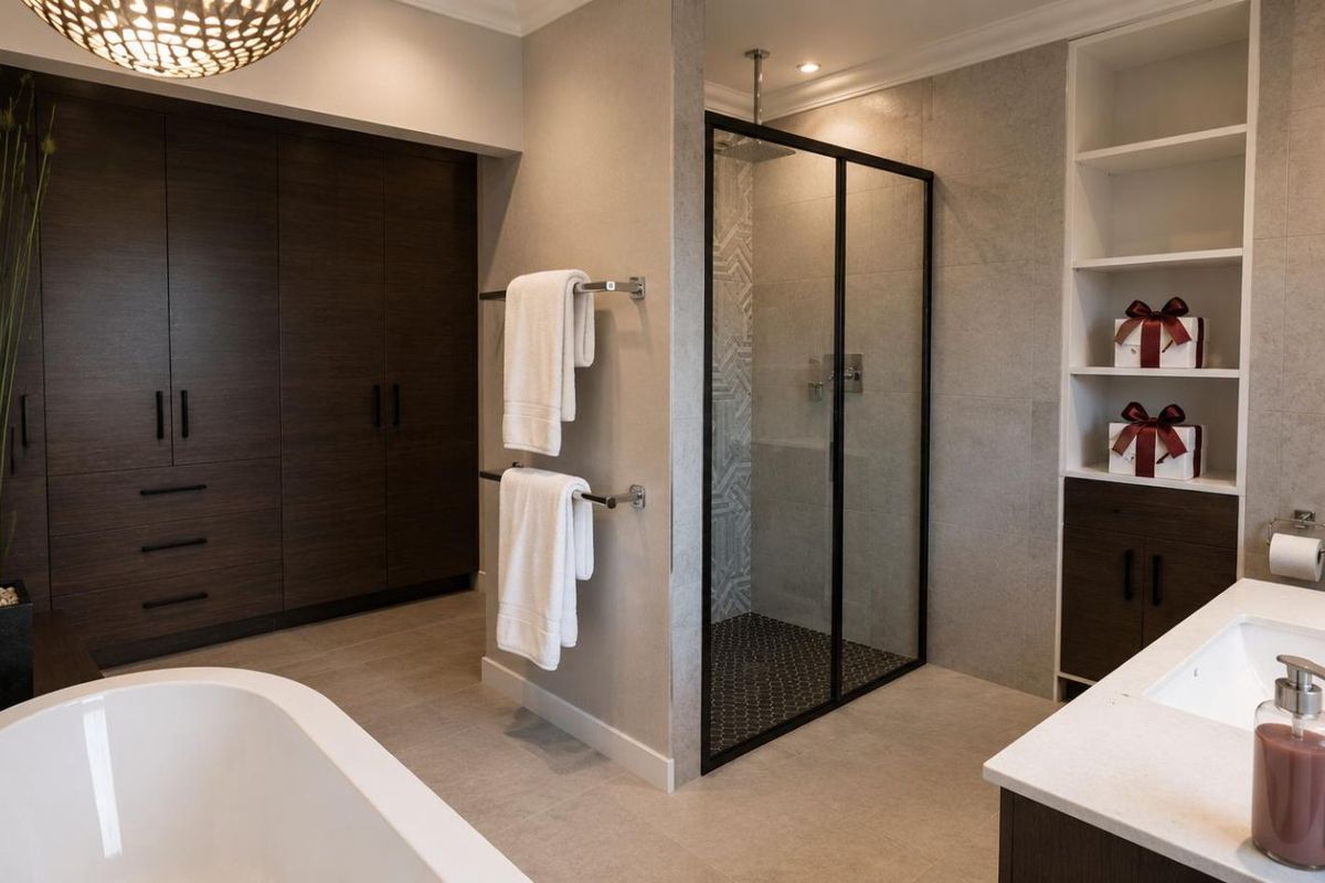 Modern bathroom featuring a freestanding bathtub, a walk-in shower with a black frame, dark wood cabinetry, and built-in shelving.