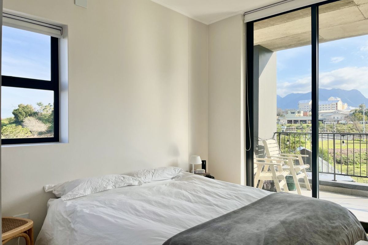 Bright bedroom featuring large sliding glass doors leading to a private balcony with scenic mountain and garden views.
