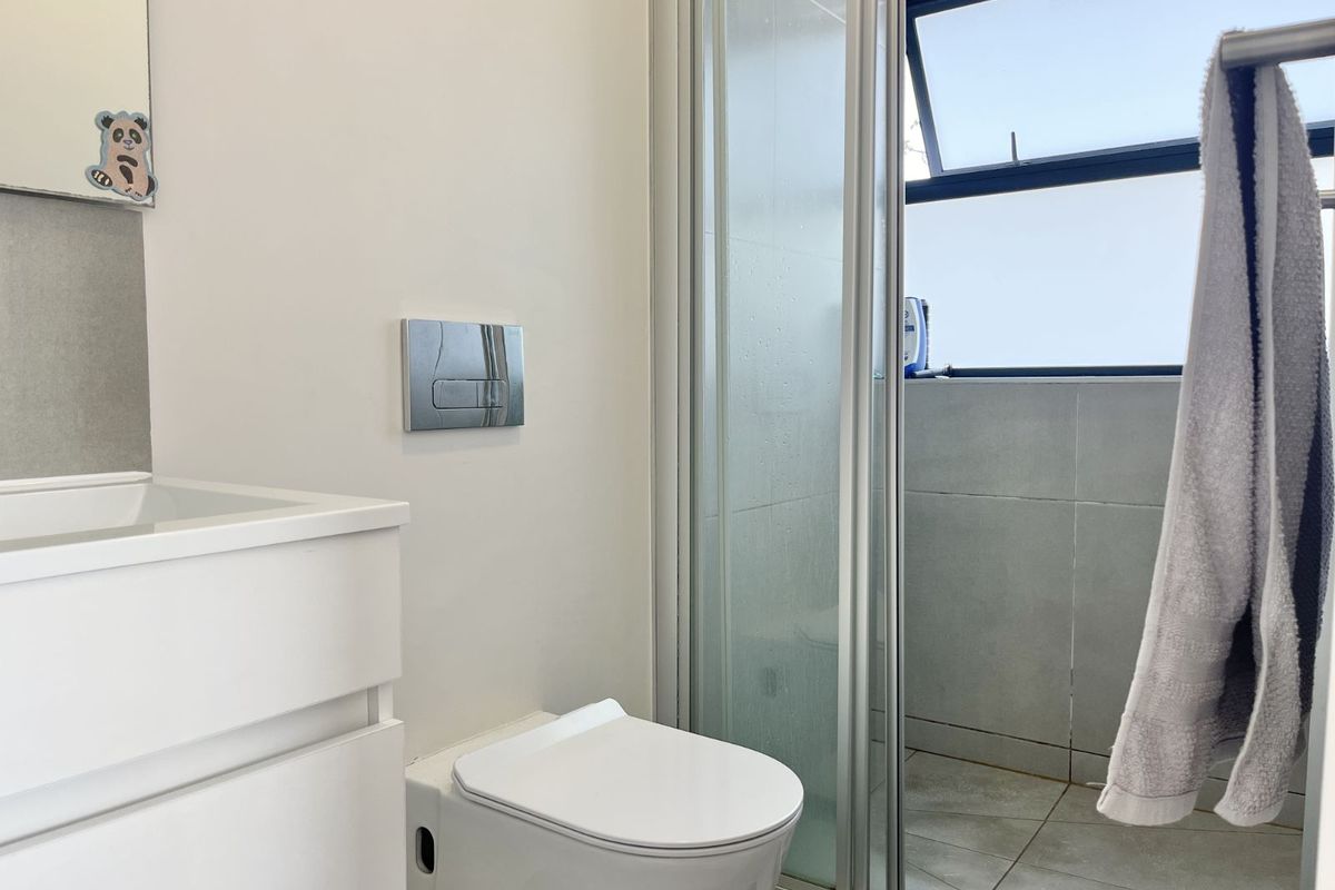 Modern bathroom featuring a wall-mounted toilet, vanity unit, and a glass-enclosed shower with grey floor and wall tiling.