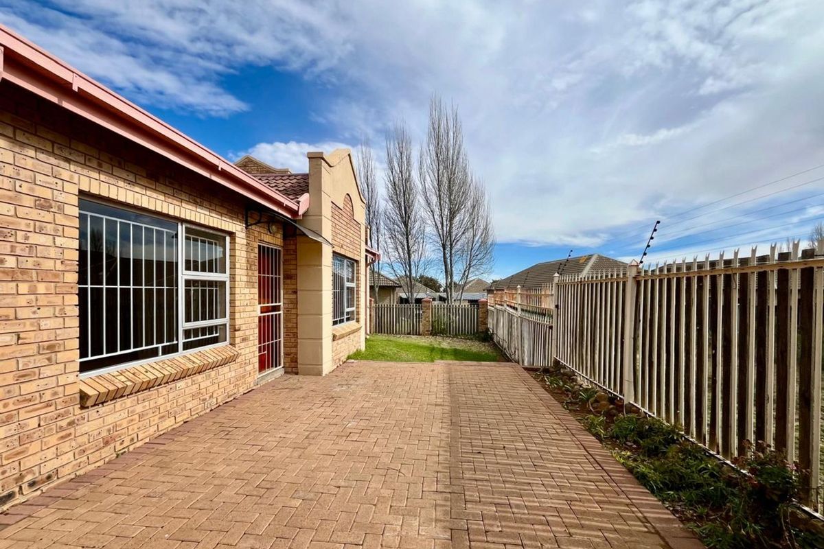 A paved rear patio area featuring face-brick exterior walls, security bars on windows, and perimeter metal fencing.