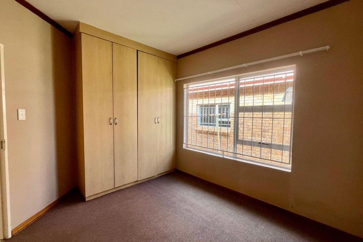 A bedroom featuring built-in wooden cupboards and a window fitted with security bars, offering a functional and private living space.