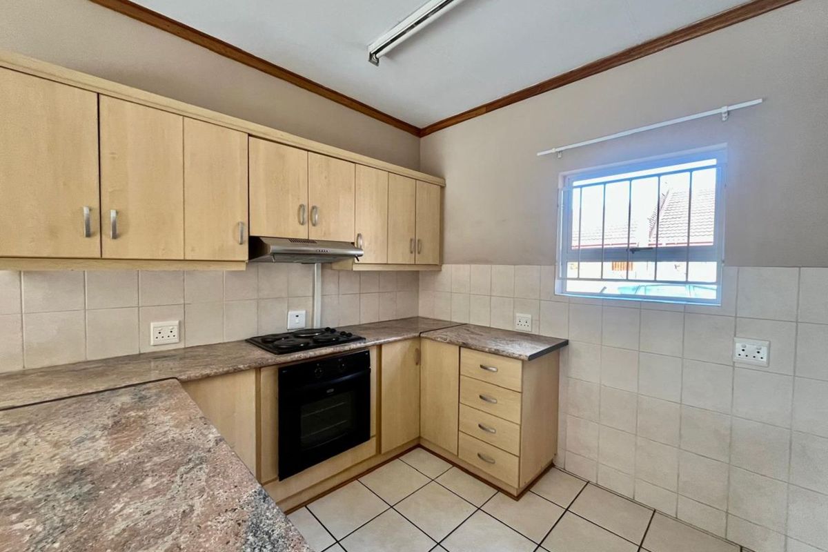 A functional kitchen featuring light wood cabinetry, granite-look laminate countertops, a built-in oven and hob, and tiled flooring.