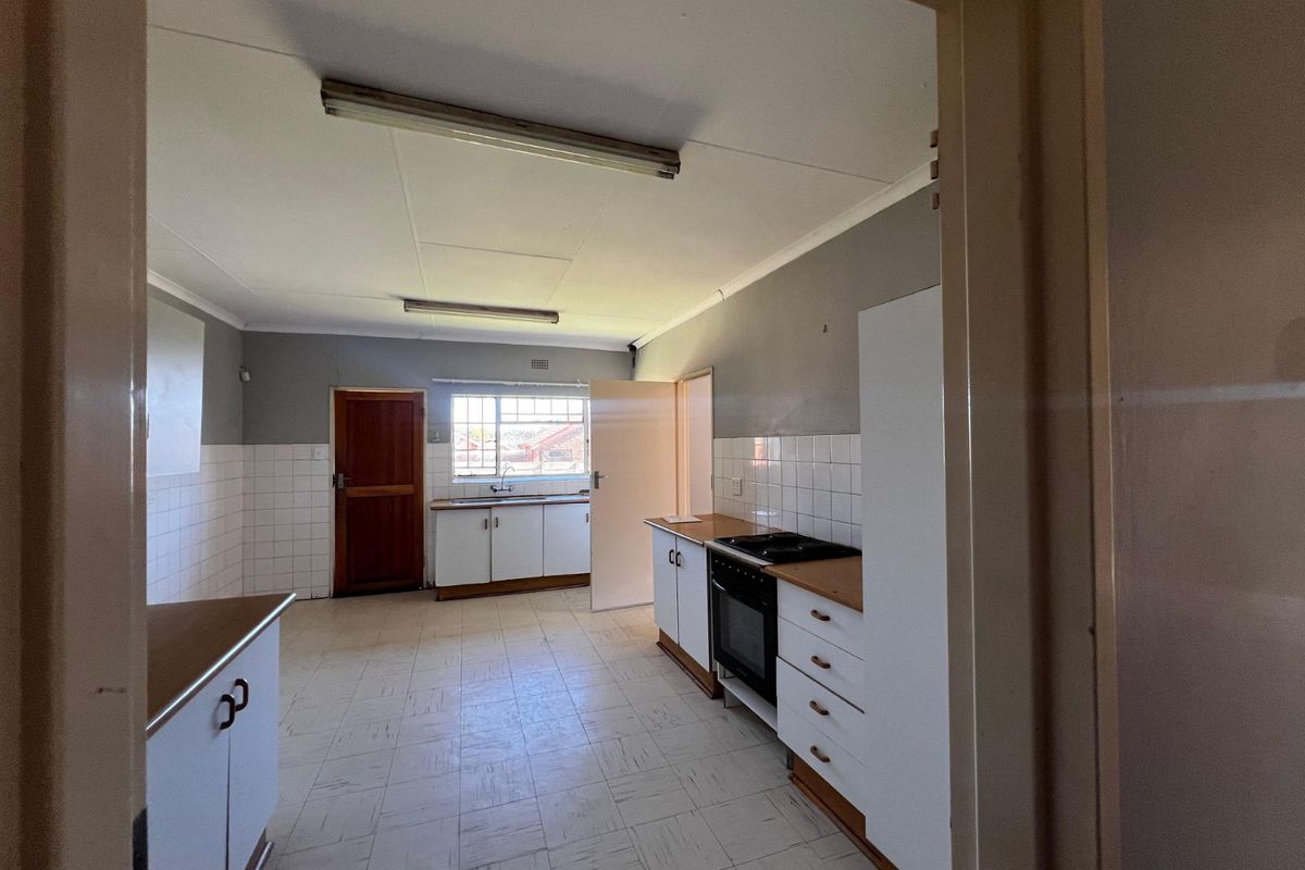 A dated, functional kitchen featuring white cabinetry, tiled splashbacks, and a built-in oven, offering a blank canvas for potential renovation.