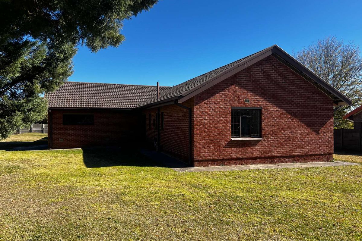 A view of the rear exterior of a red brick house featuring a tiled roof and surrounding lawn area.