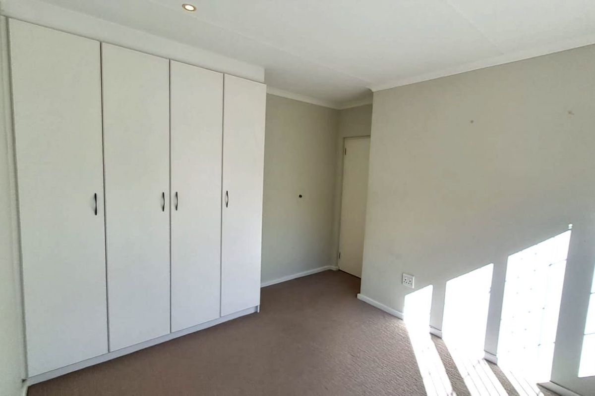 A bedroom featuring built-in cupboards and carpeted flooring, illuminated by natural light through a decorative glass block window.