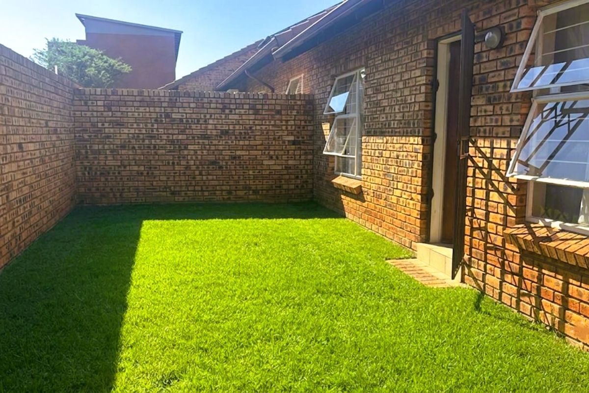 A private rear garden area featuring face-brick boundary walls, a well-maintained lawn, and direct access to the townhouse interior via a side door.