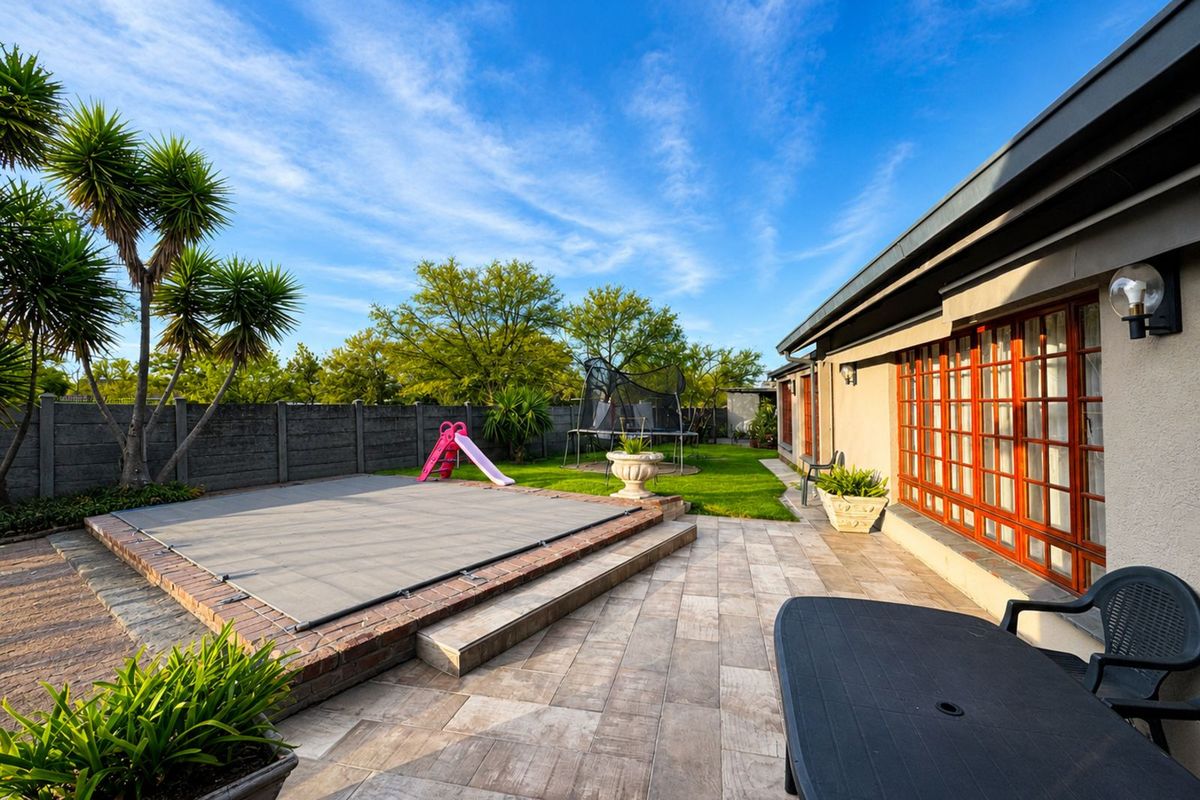 A well-maintained rear garden featuring a paved patio area, a swimming pool with a safety cover, and a lawned backyard.