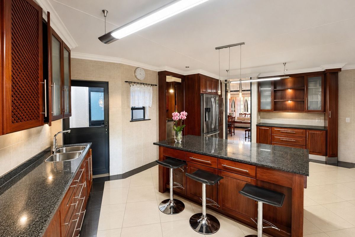 Spacious kitchen featuring dark wood cabinetry, granite countertops, a central island with breakfast bar seating, and tiled flooring.