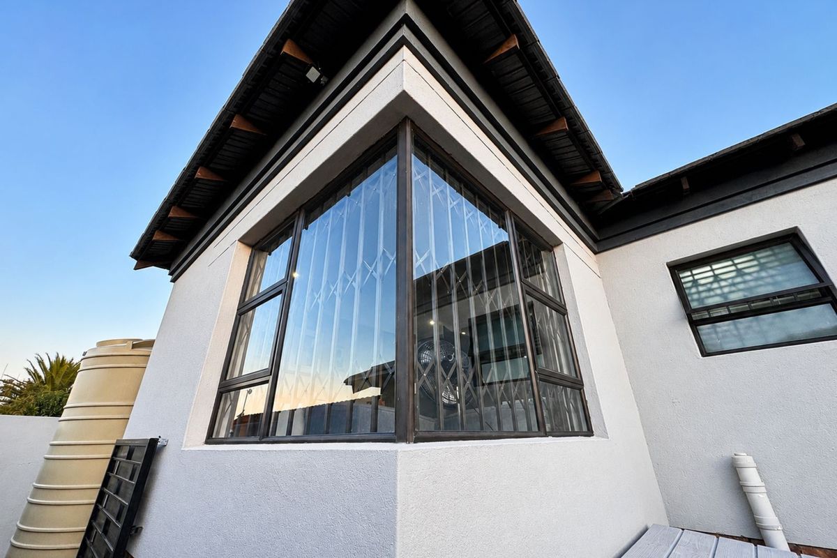 Exterior view of the property featuring modern corner windows with security bars, a water storage tank, and a clean rendered facade.