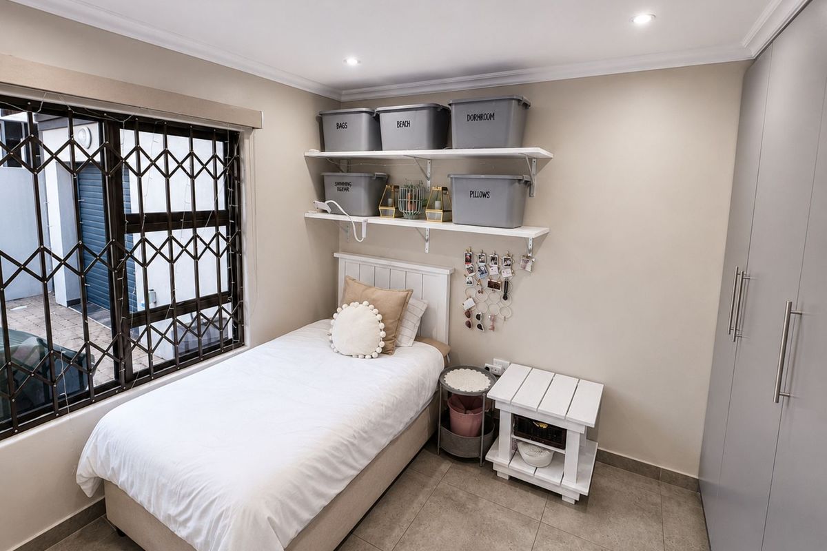 A compact bedroom featuring tiled flooring, built-in floor-to-ceiling wardrobes, and a window fitted with a security gate.
