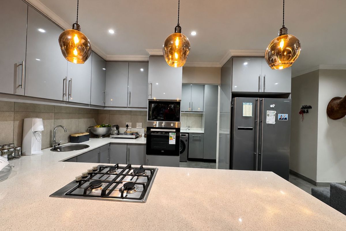 Modern kitchen featuring sleek grey cabinetry, stone countertops, a built-in gas hob, and integrated oven, with an adjacent scullery area.