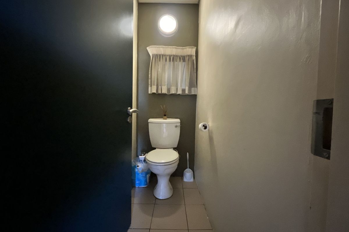 A compact guest bathroom featuring tiled flooring, a standard toilet, and a wall-mounted light fixture.
