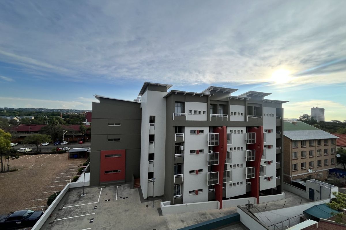 An elevated exterior view of a modern multi-story apartment building featuring a contemporary facade with balconies and adjacent paved parking area.