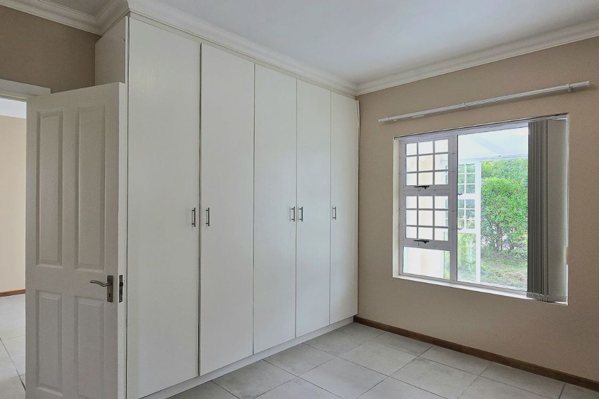 A bright bedroom featuring built-in white cabinetry, tiled flooring, and a window with garden views.