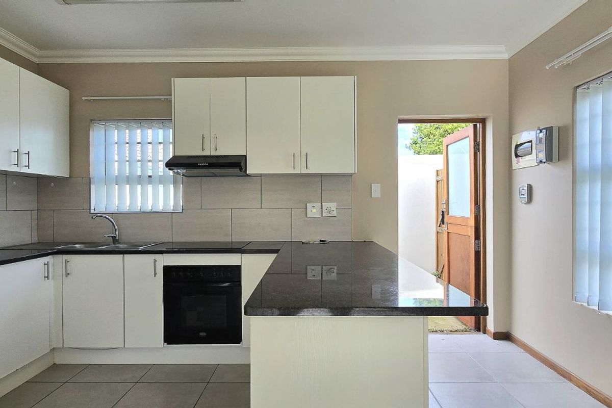 A functional kitchen featuring white cabinetry, dark granite countertops, a built-in oven, extractor fan, and tiled flooring with direct access to the exterior.